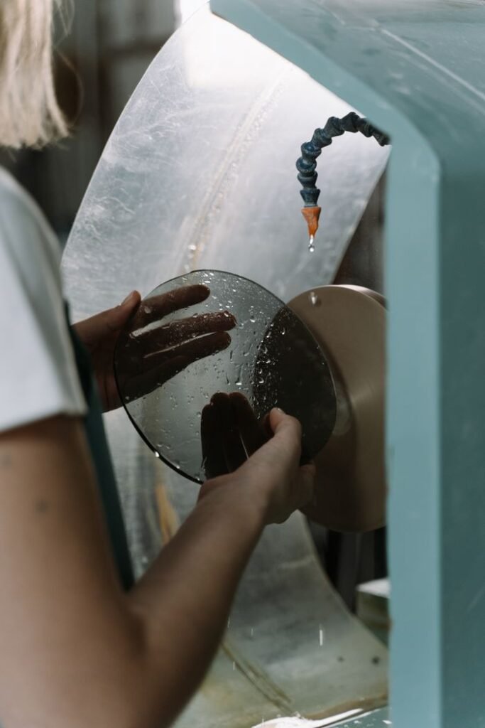 Worker using machine to cut and shape glass. Industrial craftsmanship captured in detail.